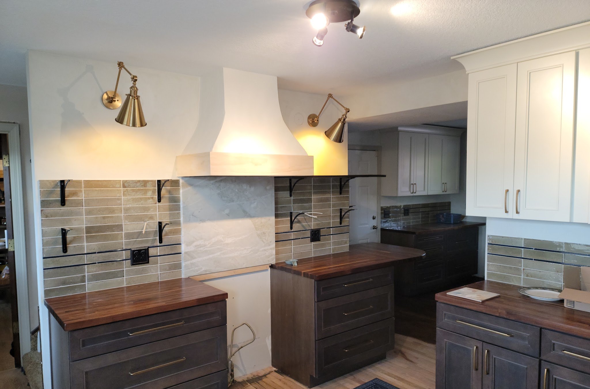 Finished kitchen with tiled backsplash, plaster range hood, brass wall sconces and butcher-block counters